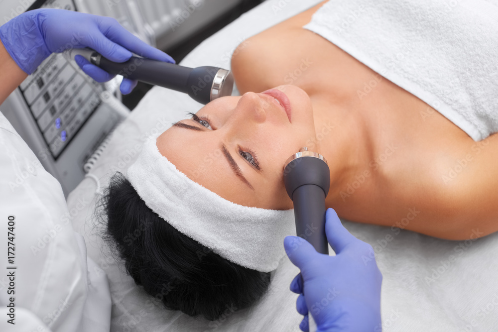 Φωτογραφία The cosmetologist makes the procedure an ultrasonic cleaning of the facial skin of a beautiful, young woman in a beauty salon