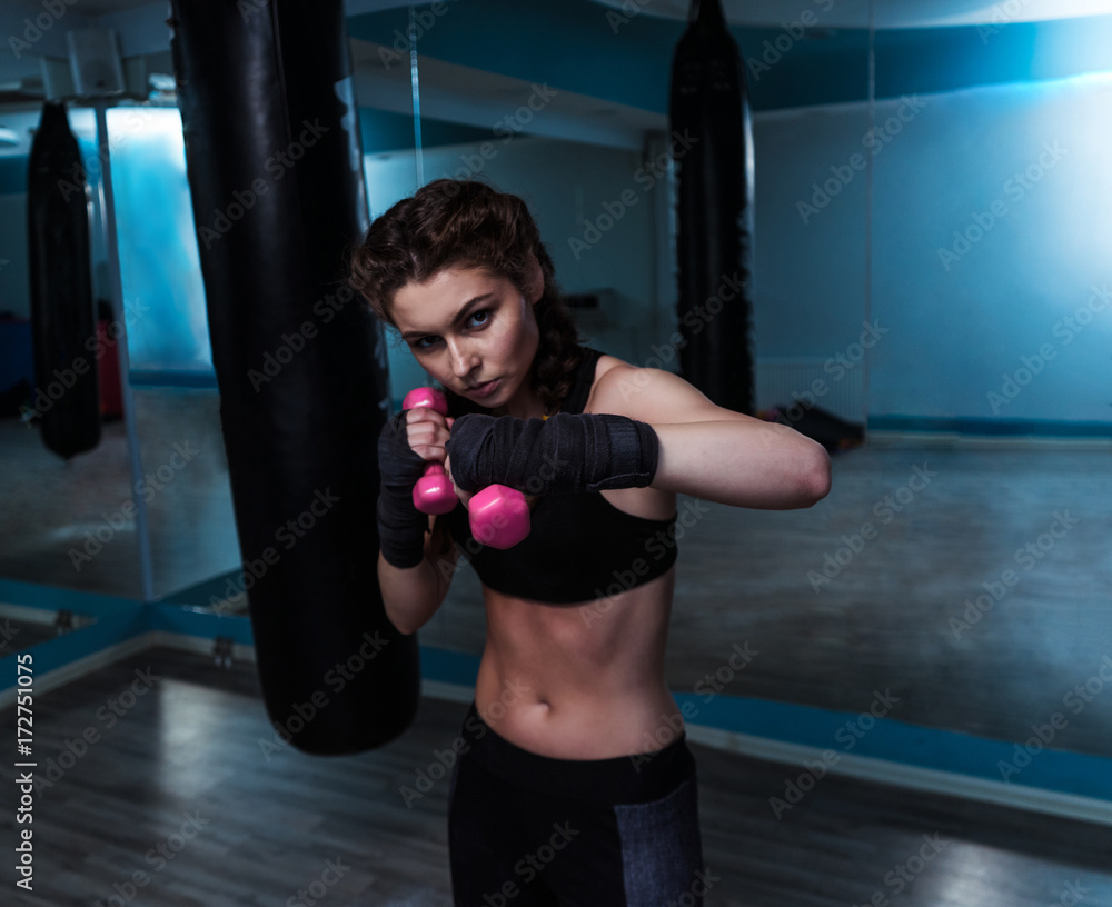 Young fighter boxer fit girl with hand bandage in training with pink dumbbells. Woman power and beauty