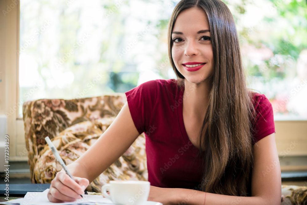 Young woman looking at camera while writing indoors in cafe Young woman looking at camera while writing indoors in cafe