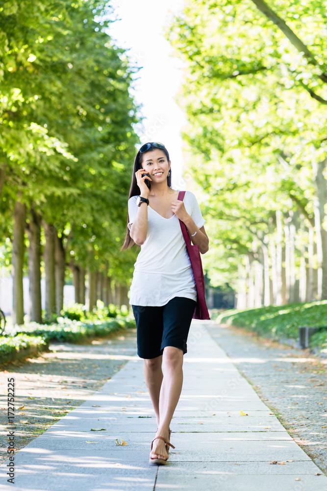 Obraz premium Young Asian woman talking on mobile phone outdoors in the park