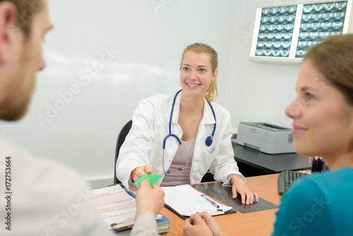 young couple giving social insurance card to female doctor