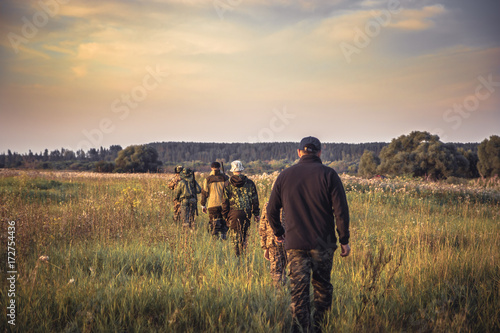 Group of people in a row going away through rural field at sunset during hunting season in countryside