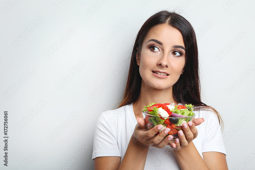 Young woman with vegetable salad in glass bowl on grey background Young woman with vegetable salad in glass bowl on grey background