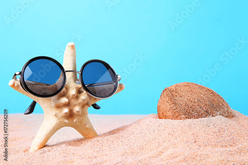 Coconut with starfish in sunglasses on the beach sand