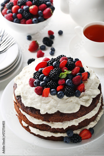Delicious chocolate biscuit cake with berries and cup of tea on white wooden table