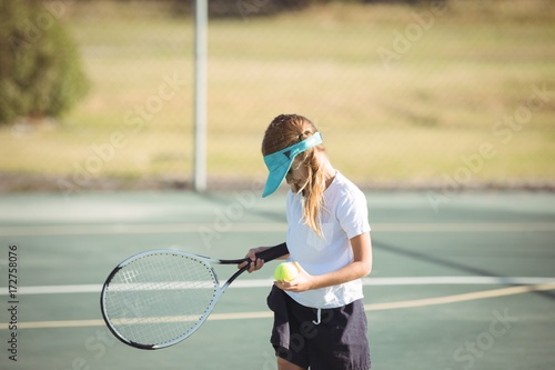 Girl holding tennis ball and racket on court