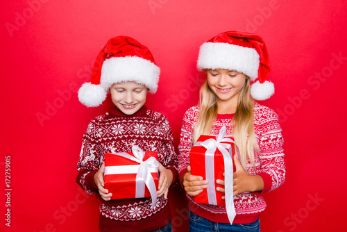 Small adorable charming relatives in traditional x mas clothing  isolated on red background  excited  looking at gifts  hold them and guess what s inside  curiousity  wish  dream  imagination concept