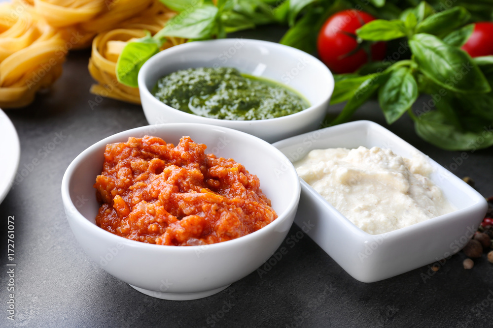 Delicious pesto, bolognese and white sauces for pasta in bowls on table