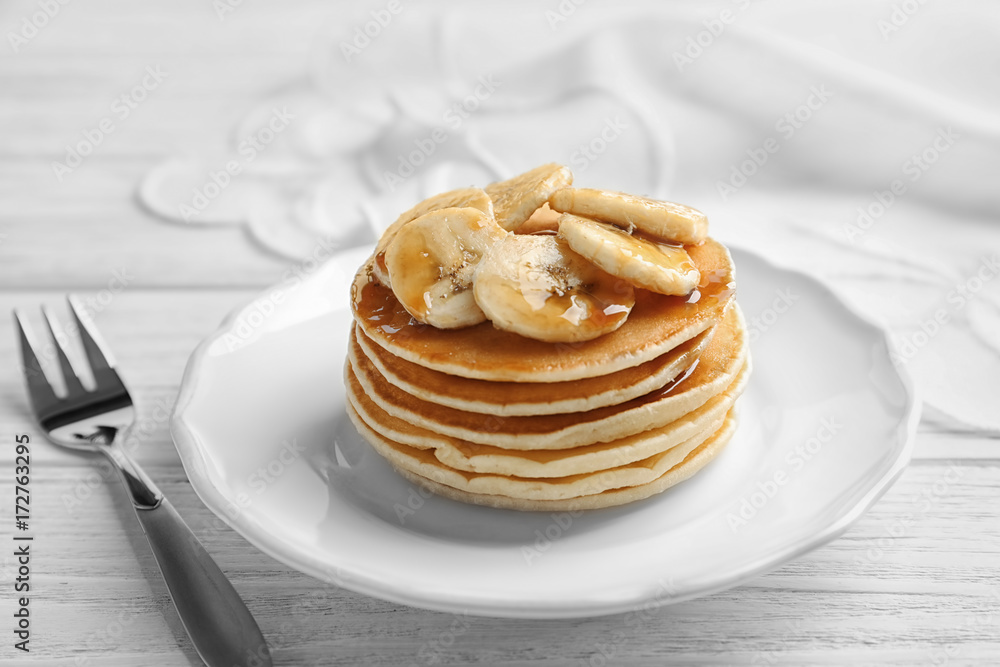 Plate with yummy banana pancakes on wooden table