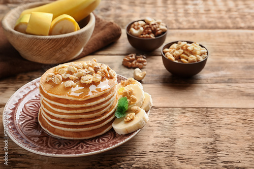 Plate with yummy banana pancakes on wooden table