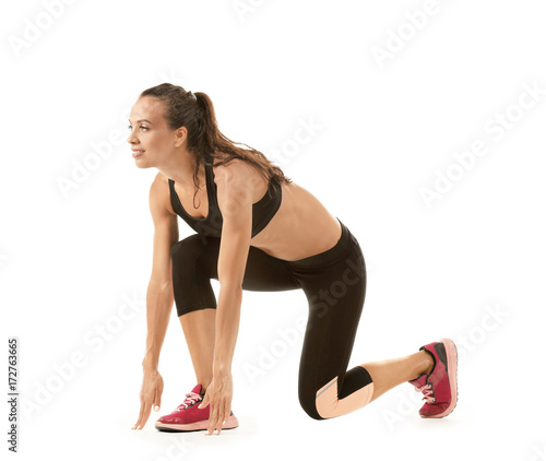 Beautiful young woman in sportswear preparing to run, on white background