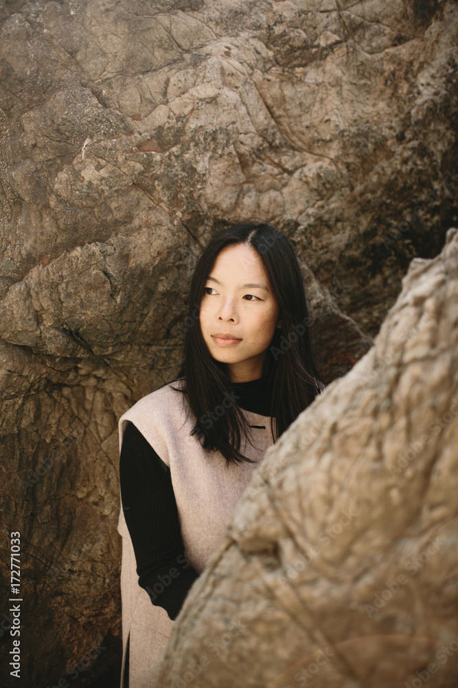 fashionable asian woman standing between rocks on coast fashionable asian woman standing between rocks on coast