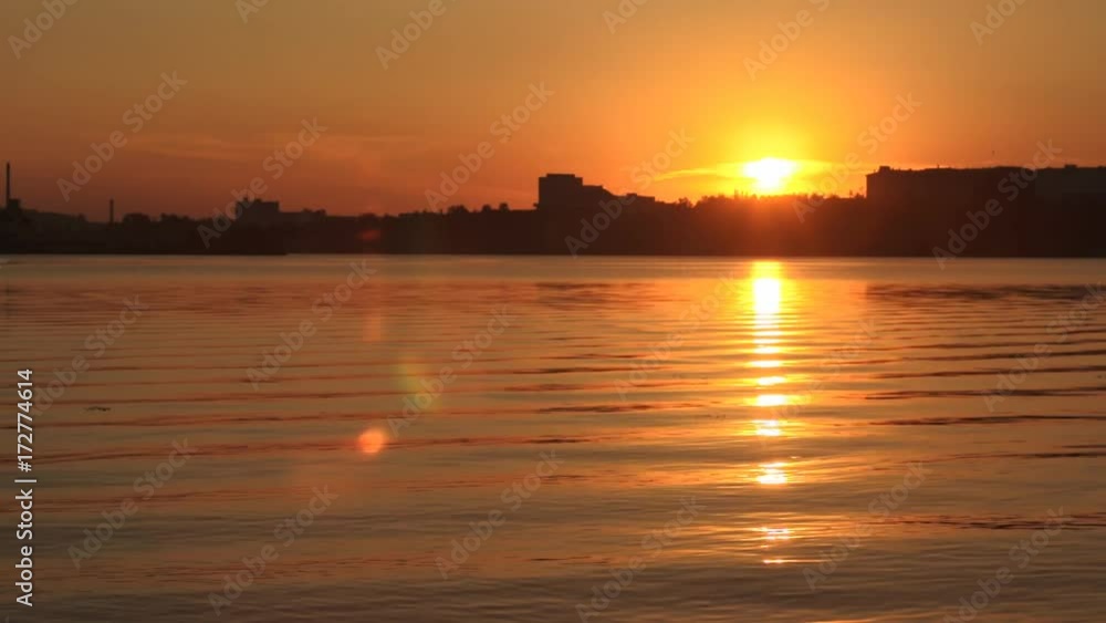 The sun sits outside the city, the sun's rays are reflected in the city pond or river. Golden glare on the surface of the water. The sun sits outside the city, the sun's rays are reflected in the city pond or river. Golden glare on the surface of the water.