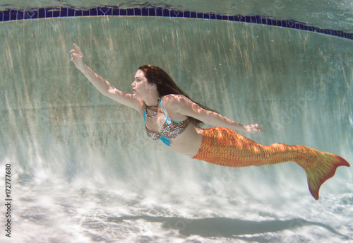 A mermaid with and orange tail underwater.