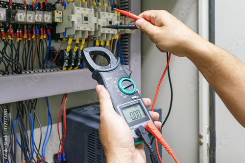 Electrical Engineer adjusts electrical equipment with a multimeter tester in his hand closeup. Professional electrician in electric automation cabinet