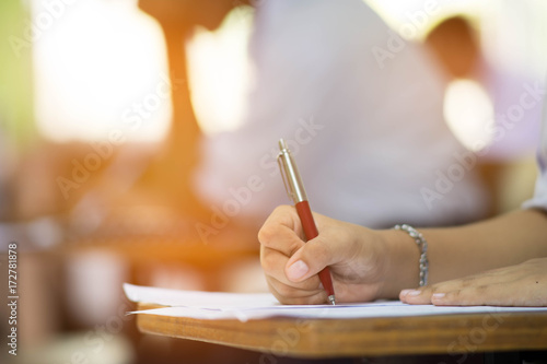 Closeup to hand of student holding pen and taking exam in classroom with stress for education test .