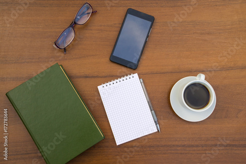 Cup of coffee  book  notepad  pen  eyeglasses and smart phone on wooden desk