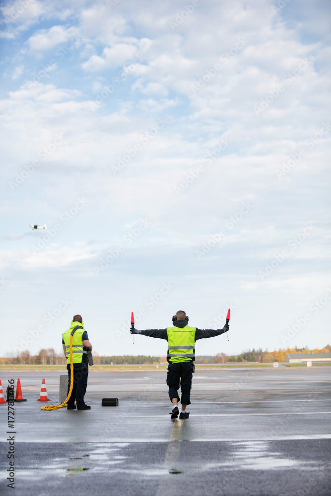 Obraz premium Marshaller Holding Signal Wands While Standing By Colleague On R