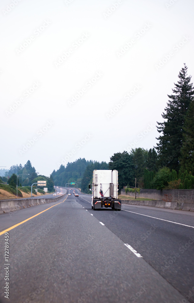 WHite semi truck tractor running on devided freeway with green trees