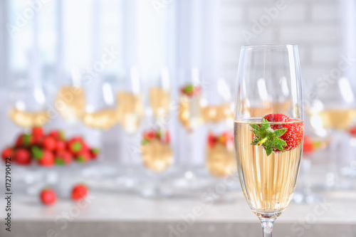 Glass of delicious wine with strawberry on blurred background