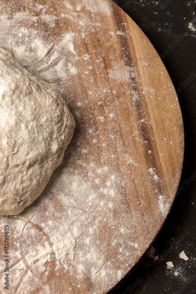 Ball of dough on a rustic wooden board with dusting of flour. Black background Ball of dough on a rustic wooden board with dusting of flour. Black background