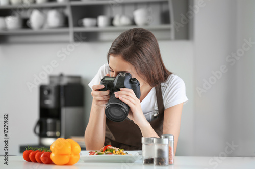 Young female blogger making photo of freshly cooked dish in kitchen