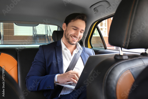 Handsome man with laptop sitting in taxi car © Africa Studio
