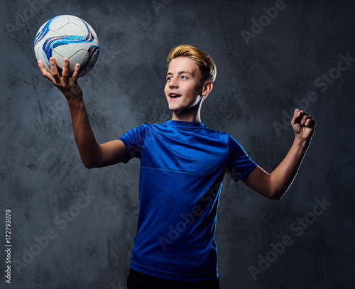 Teenager soccer player dressed in a blue uniform holds a ball.