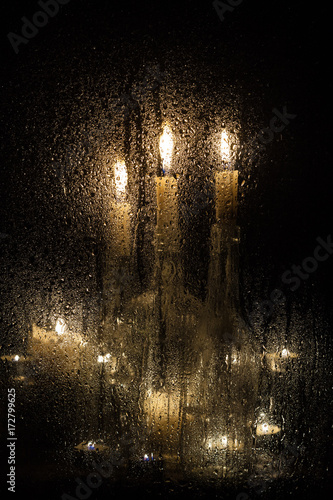 Candles and bottles behind a wet glass on a dark background.