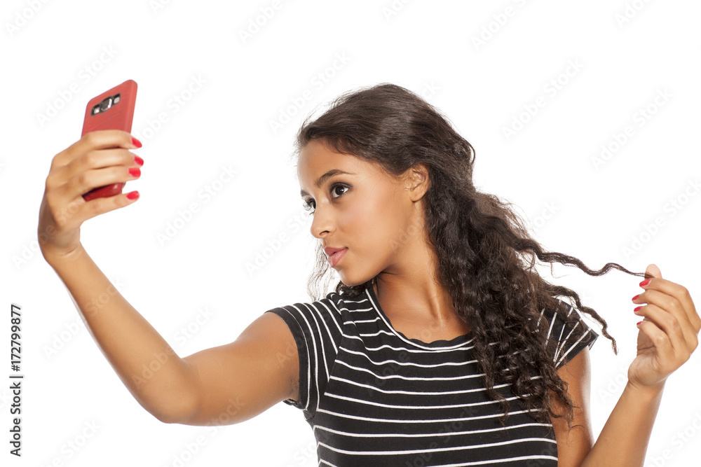 Naklejka premium Young and beautiful dark skinned girl taking a selfies with her smartphone
