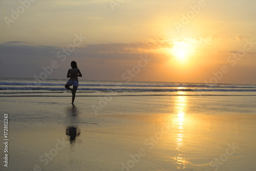 woman meditating and thinking peacefully in yoga pose on desert beach on sunset in meditation and freedom