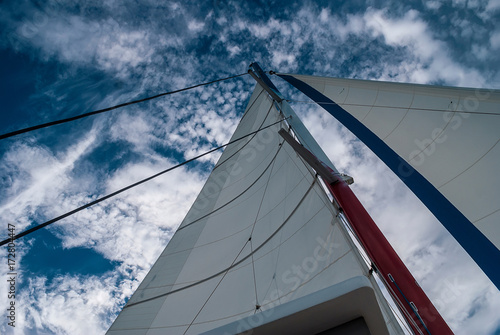 The mast and sails recreational catamaran on a background of cloudy sky.