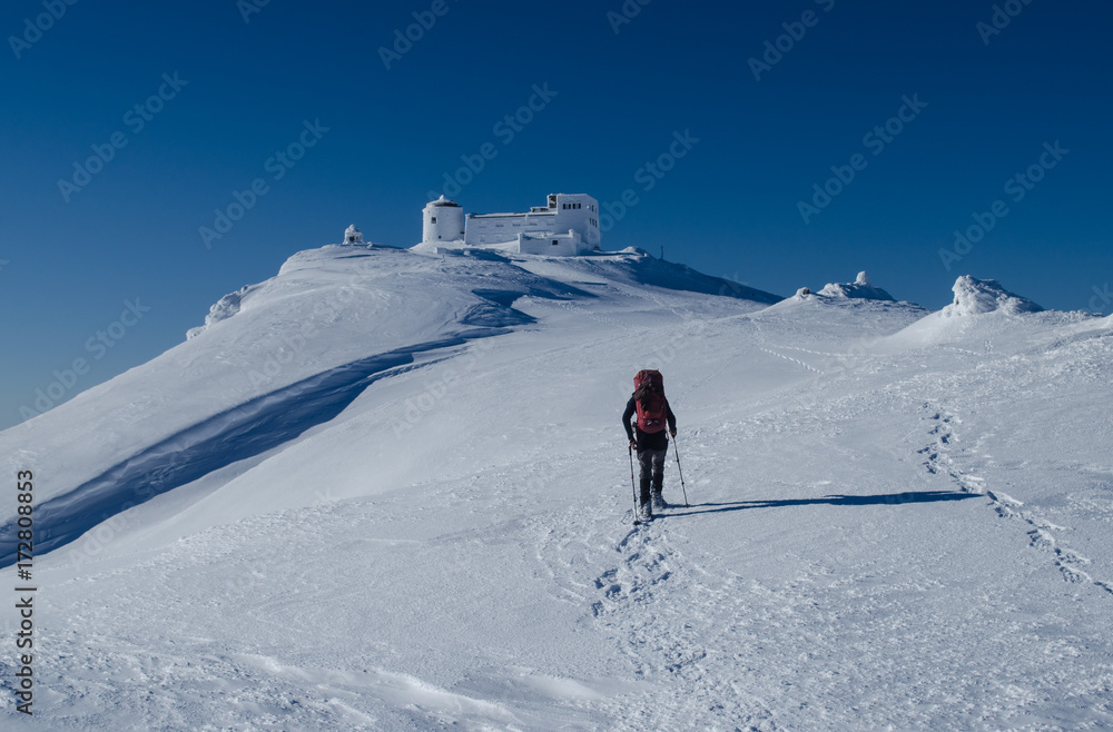 Winter picture of a hiker walking towards the abandoned observatory atop the mountain Pip Ivan in Ukrainian Carpathians