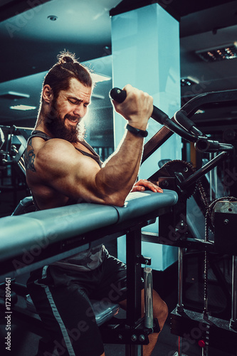 Bearded Man Doing Heavy Weight Exercise For Biceps On Machine In A Gym