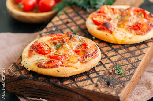 Mini pizzas margheritas on served on a wooden board. Black stone background