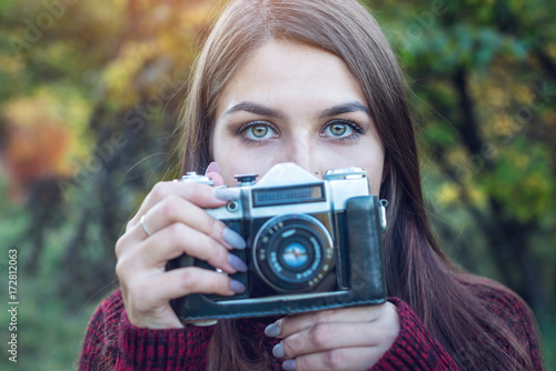 Beautiful woman in autumn Park holds vintage retro camera. Concept of photography as a hobby