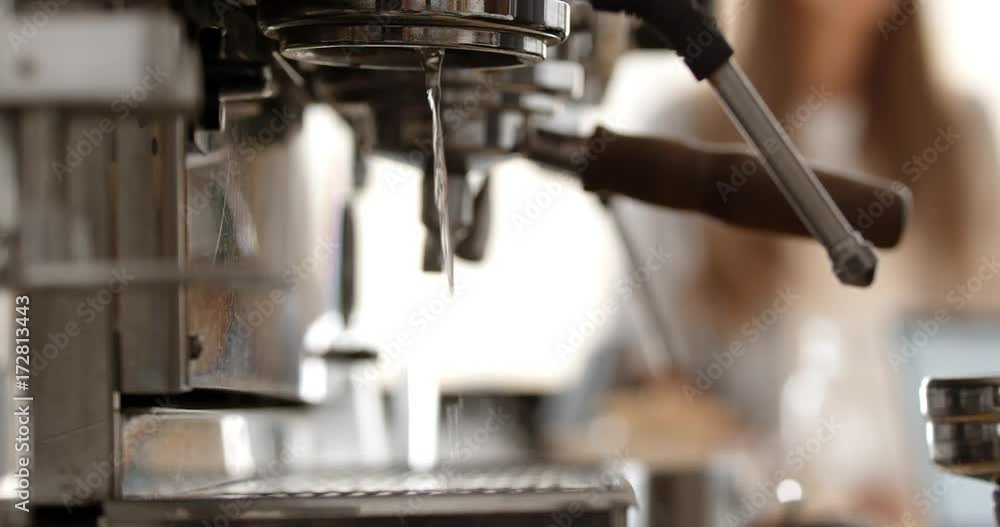 Barista preparing two espressos on coffee machine in busy cafe, skimming milk. Close up. Slow motion.