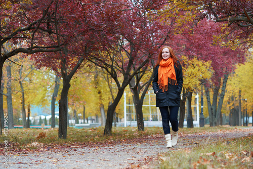 young woman walk on footpath in autumn park, yellow leaves and trees