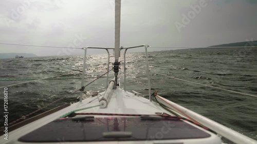 Slow motion view of coastline, stormy water of river and boats on it. View from sailing yacht board photo