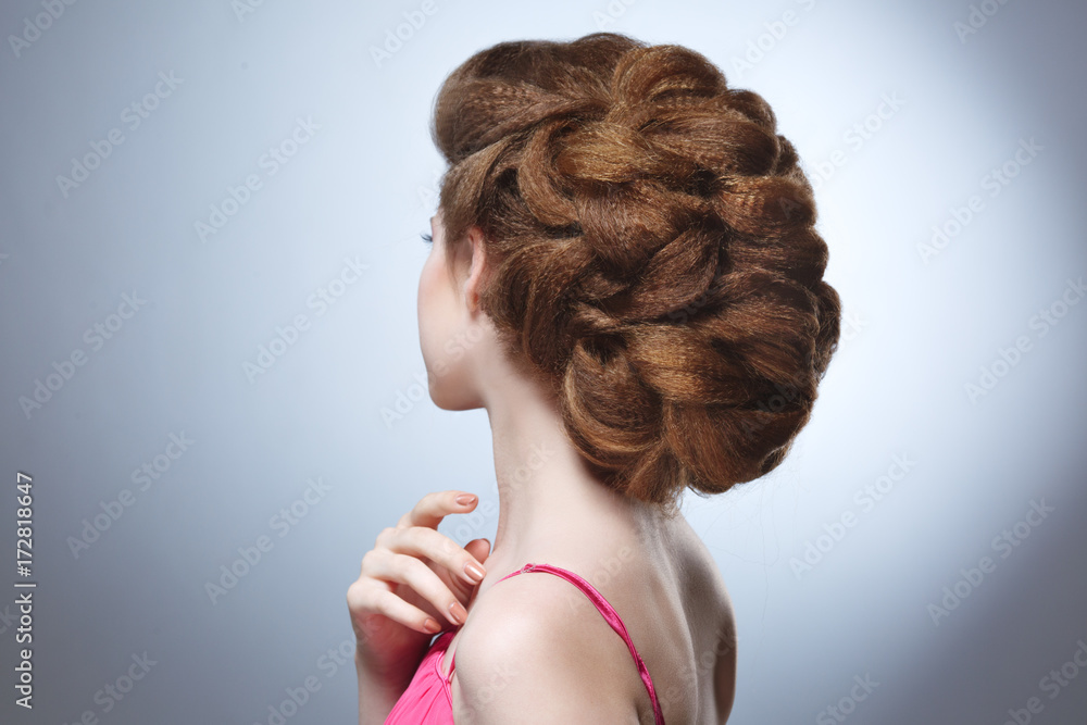 Beauty portrait of a girl with a voluminous hairdo from the back against a gray background.