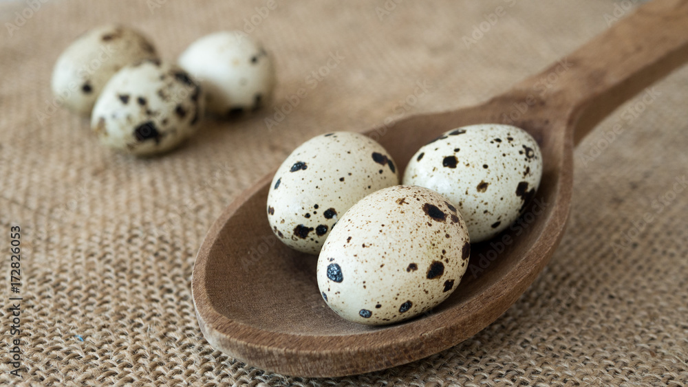 Three quail eggs in wooden spoon on jute burlap Three quail eggs in wooden spoon on jute burlap