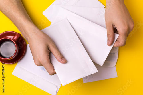 A man sorts the mail. Male hands the envelopes on a yellow background, a red coffee Cup.