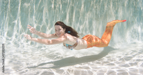 A mermaid with and orange tail underwater.