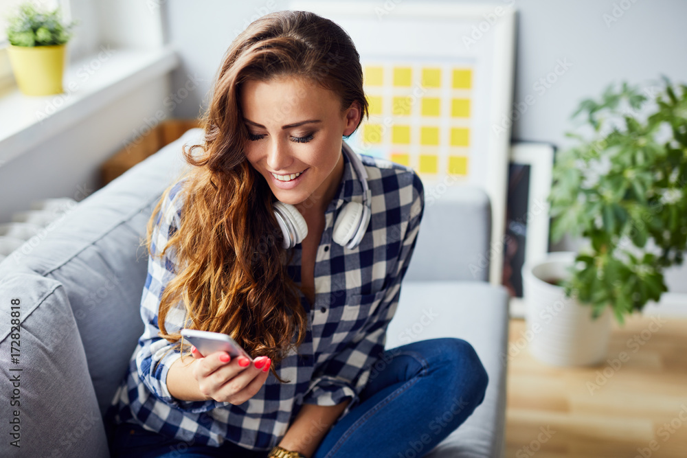 Cheerful pretty young woman sitting on sofa at home, laughing and using phone Cheerful pretty young woman sitting on sofa at home, laughing and using phone