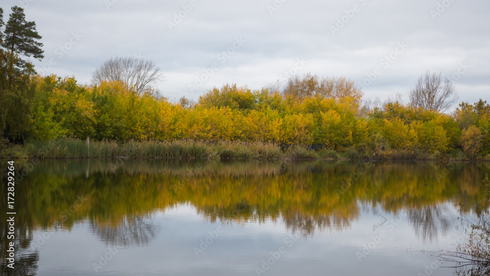 A small lake in the Park, the yellowing trees along the shore. The reflection of sky and trees in the water of the lake. A beautiful scenic place A small lake in the Park, the yellowing trees along the shore. The reflection of sky and trees in the water of the lake. A beautiful scenic place