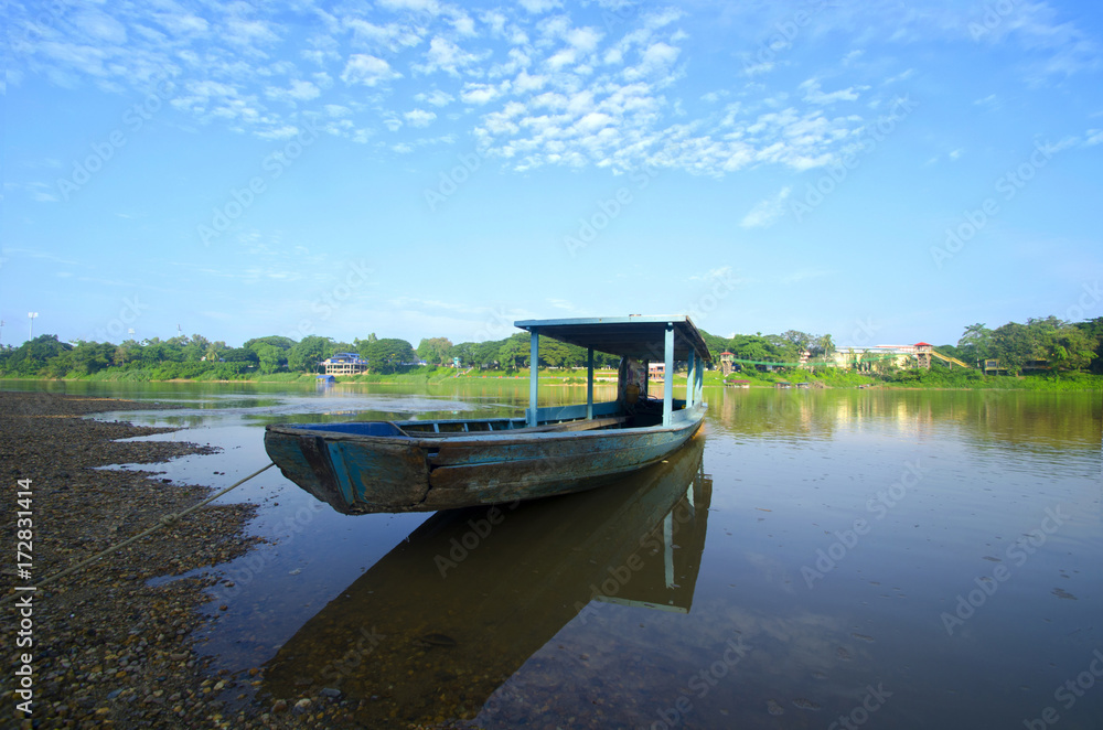 Fototapeta premium Old Blue boat nearby a river at beautiful summer sunrise
