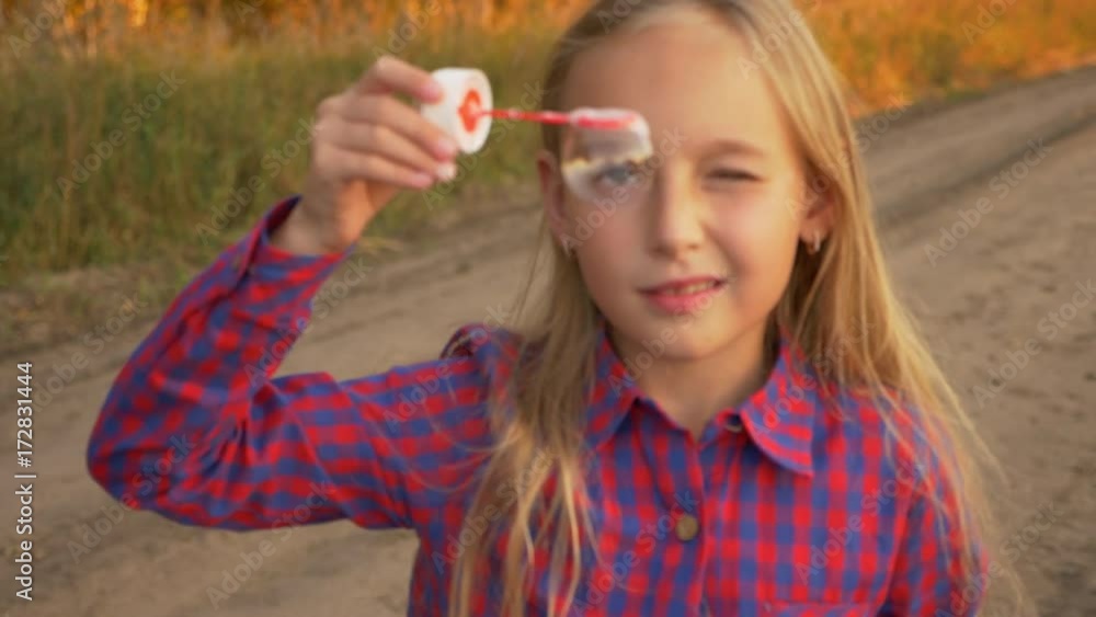 Close up view young girl looking through soap-bubble outdoors. From unfocused foreground to focus.