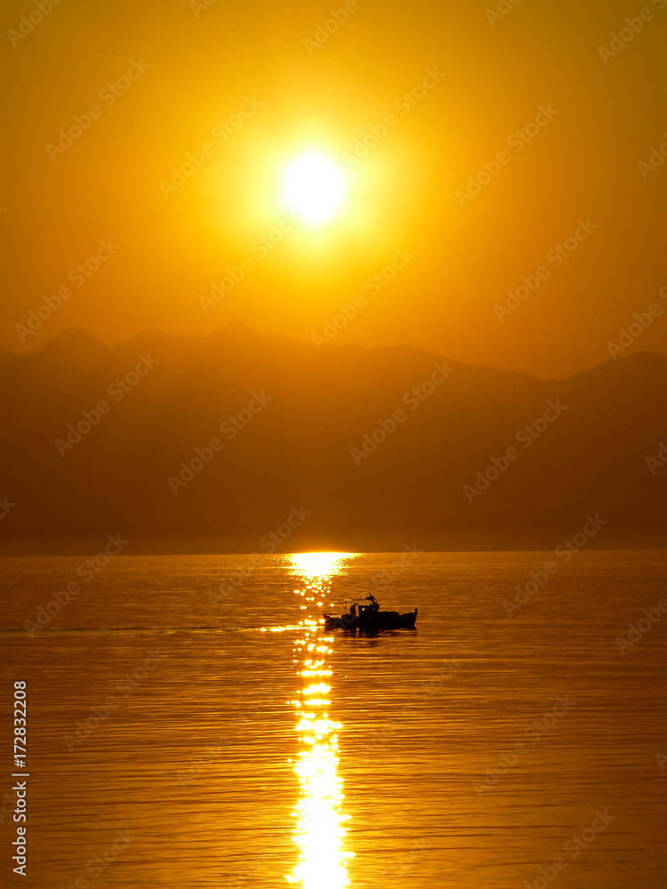 Golden sunrise with boat on the Aegean sea, mountain background.