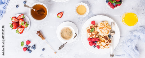 Flat lay with breakfast with scotch pancakes in flower form, berries and honey on light wooden table. Healthy food concept. Banner.