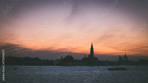 Italian silhouette of Venice at sunset with boats, Italian city panorama vintage shot from sea and sky, Sunset in Venice background, Dark scene of Venice skyline, Symbol of evening Venice © marvlc